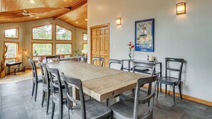Une grande table à manger entourée de huit chaises, un plafond en bois, de grandes fenêtres et une affiche accrochée au mur.