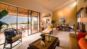 Un vaste espace de vie comprenant un grand salon avec une grande porte-fenêtre coulissante donnant sur un balcon, un coin repas et un ventilateur de plafond.