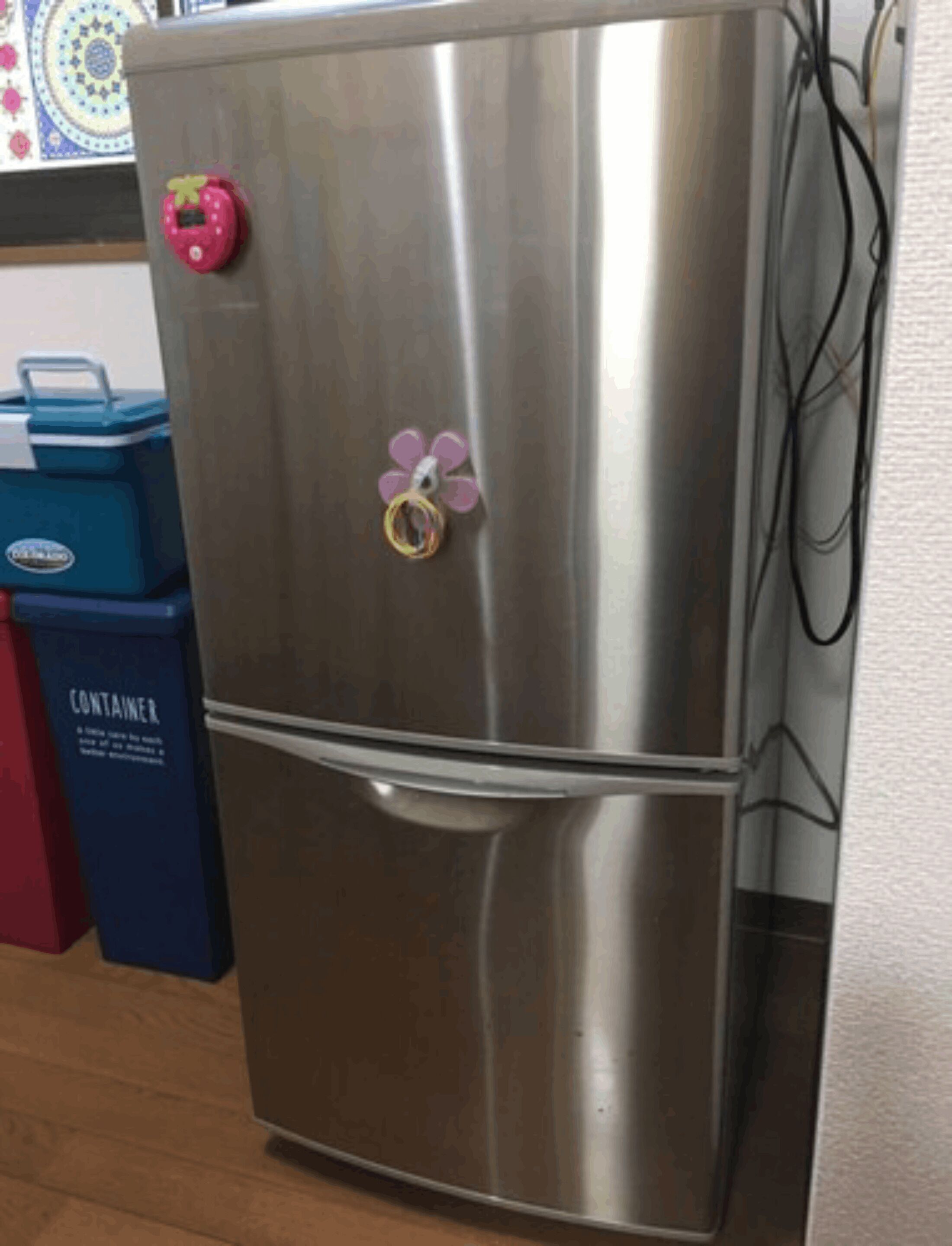 Een roestvrijstalen koelkast met een bloemmagneet in roze en paarse tinten op de deur.
