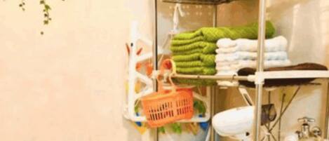 A compact bathroom with a washing machine, shelves with towels and toiletries, and a small sink.