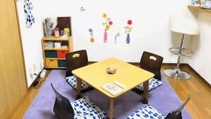 Una habitación con una mesa de madera, cuatro sillas, un tapete púrpura, una estantería y adornos en la pared.
