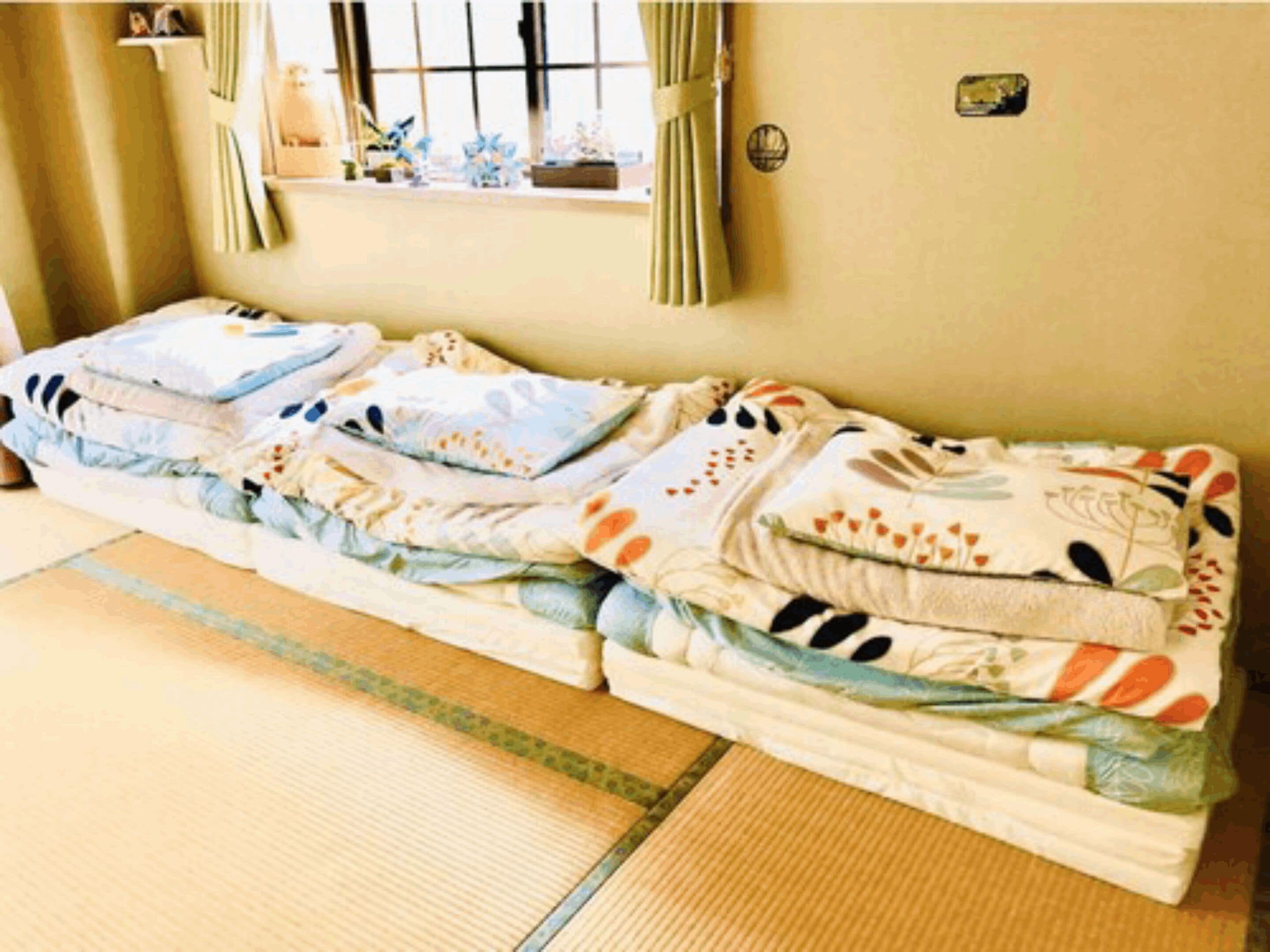 A room with a futon bed, a small window with curtains, and a wall-mounted shelf with decorative items.