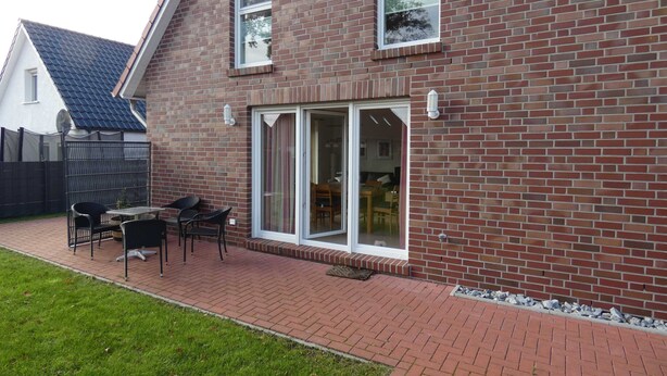 Una casa in mattoni con un patio attrezzato con tavolo e sedie, un'ampia porta scorrevole in vetro e un piccolo giardino.