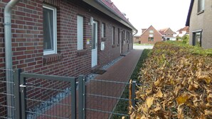 Un edificio in mattoni con tetto in tegole rosse, un ingresso con cancello e un vialetto che conduce a una fila di finestre.