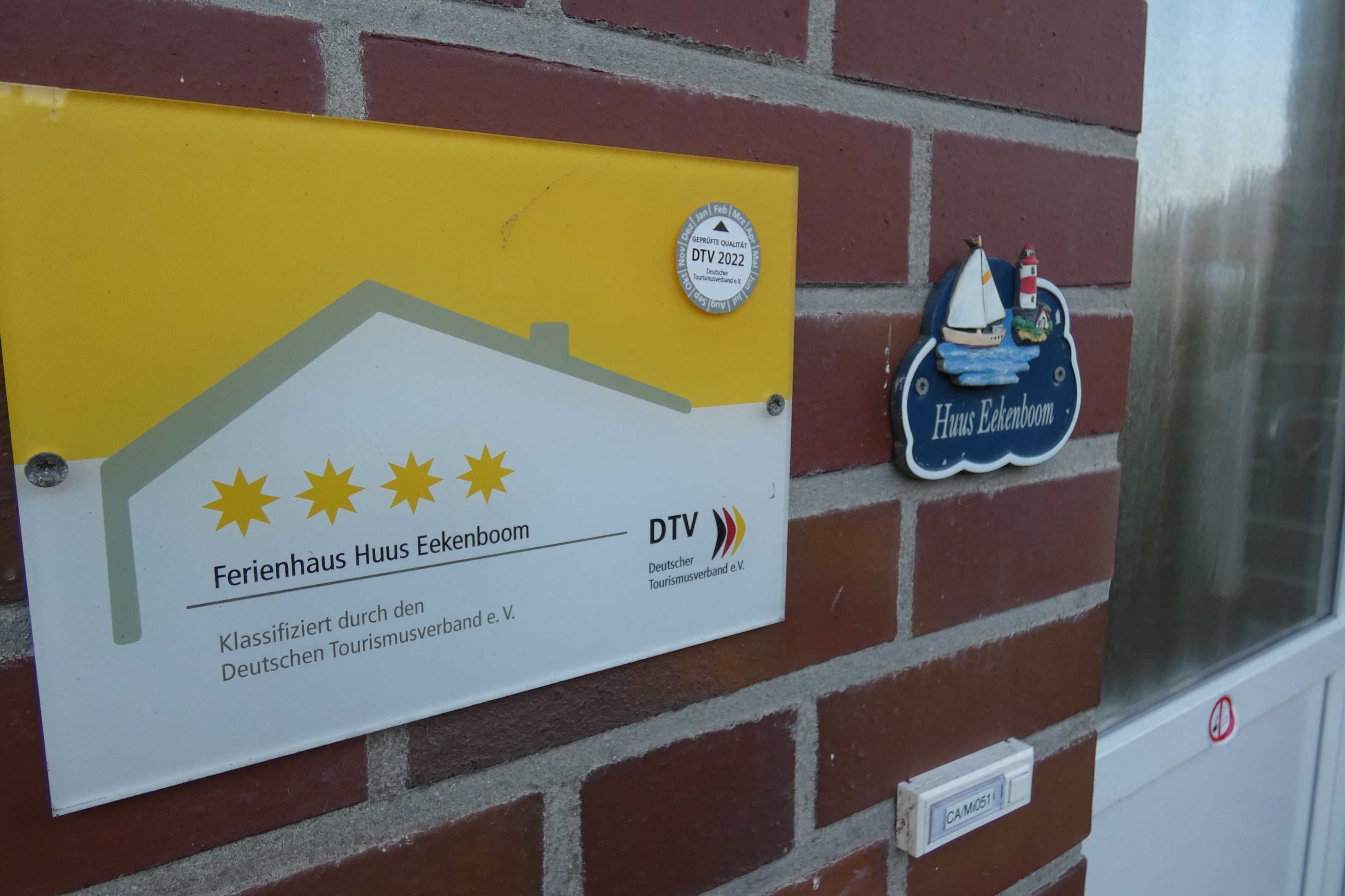 Schild für 'Ferienhaus Haus Eckenboom' mit DTV-Qualitätsabzeichen 2022, einer Sternebewertung und einer kleinen dekorativen Plakette mit Segelboot und Leuchtturm.