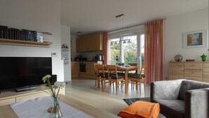 Un soggiorno moderno con una TV a schermo piatto, un'area pranzo con mobili in legno e una cucina sullo sfondo.
