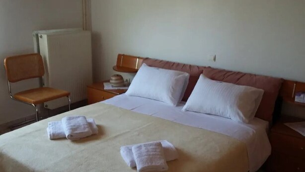 Een hotelkamer met een bed, twee kussens, een stoel, een nachtkastje en een radiator.