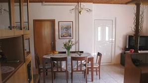 Een eetgedeelte met een ronde tafel, stoelen, een kroonluchter, een ingelijste foto aan de muur en een televisie in de hoek.