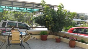 Een terras op het dak met een tafel, stoelen, plantenbakken en een geparkeerde auto.
