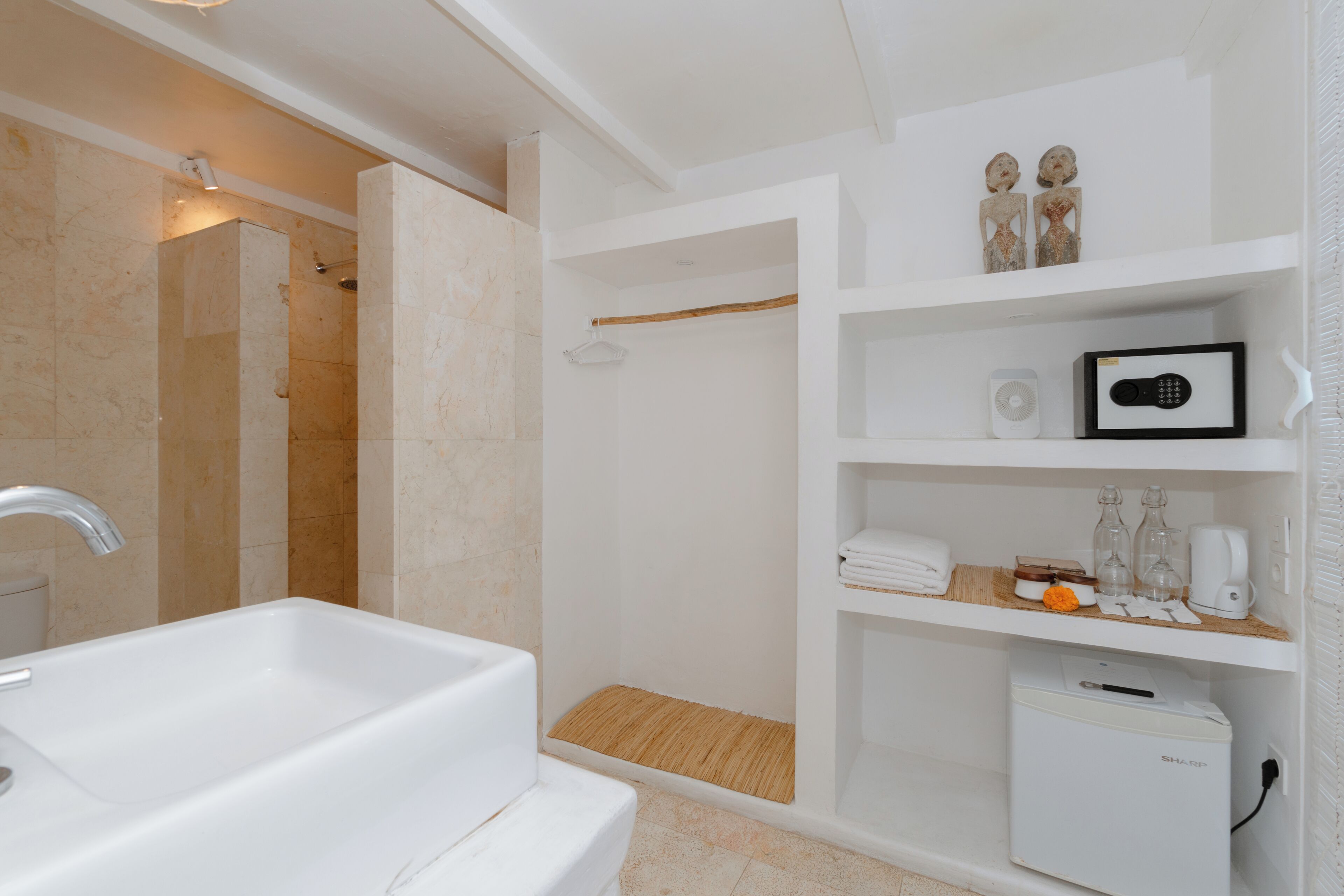 A modern bathroom with a large white sink, a shower area, and a built-in shelf with toiletries.