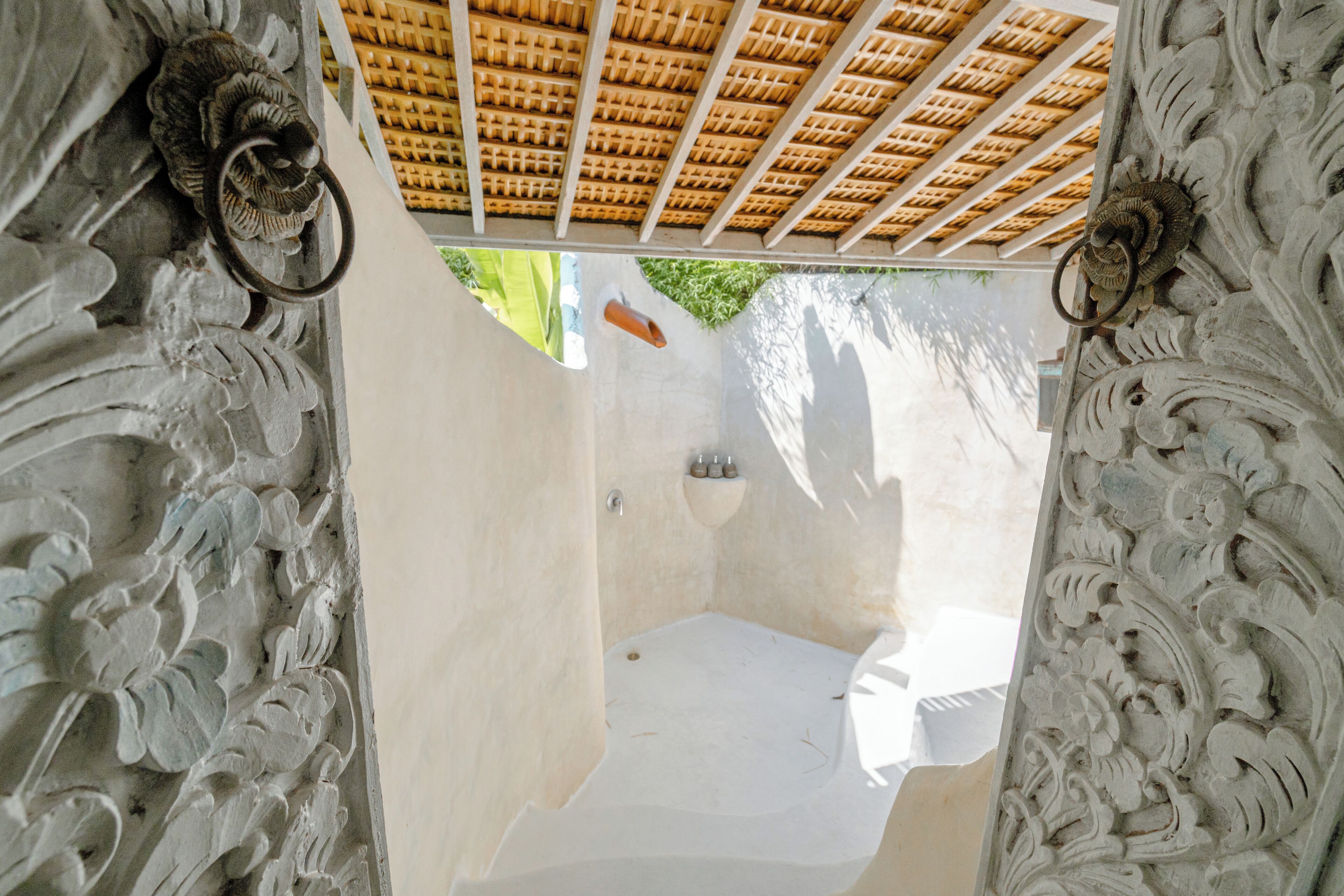 Vista a través de una puerta con adornos labrados, un techo de baldosas y una pequeña ventana.