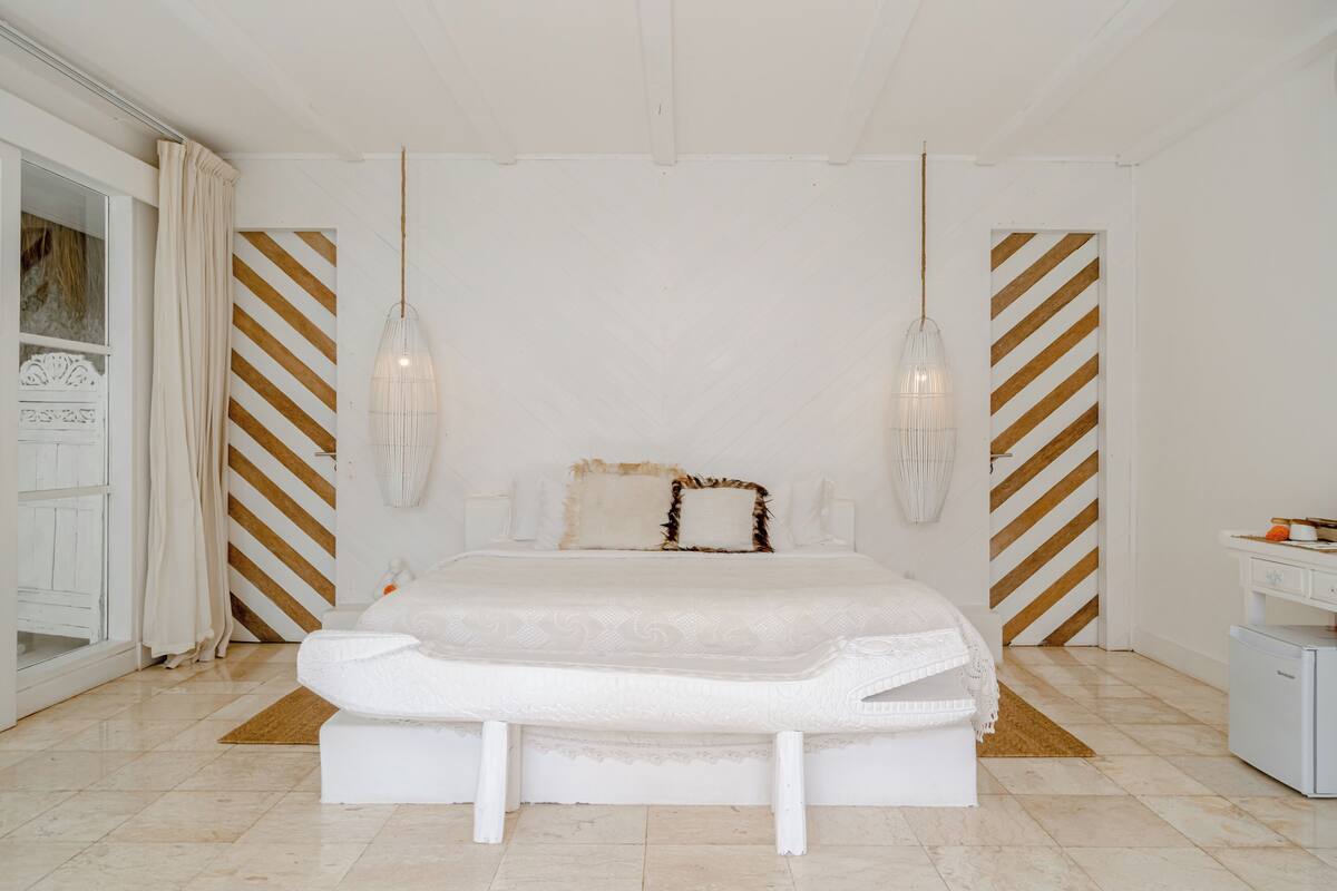 Een slaapkamer met een groot bed, twee hangende lampen en een witte dressoir.