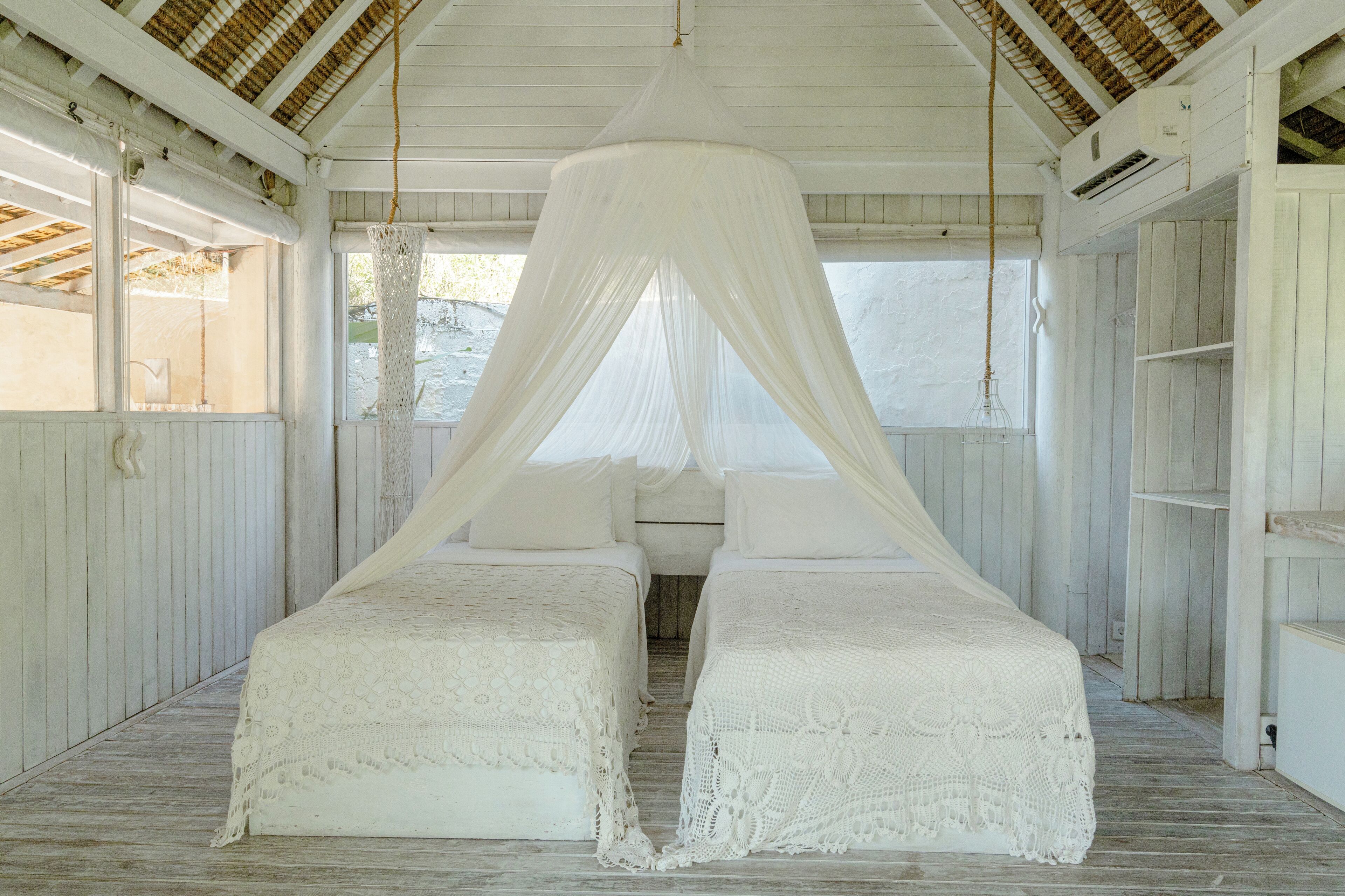 Una habitación con dos camas cubiertas con ropa blanca, cama con dosel, suelo de madera y paredes blancas.