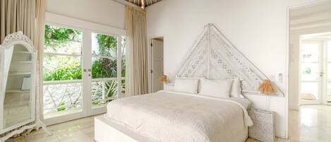 A spacious bedroom with a large bed, a decorative mirror, and a view of greenery through the sliding doors.
