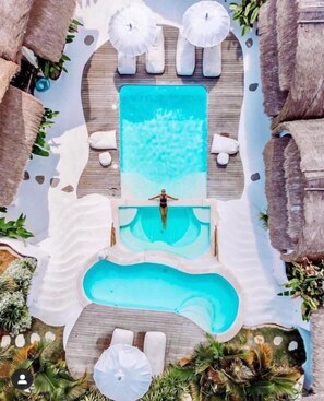 A pool area with a central rectangular pool, surrounded by lounge chairs and umbrellas, and tropical plants. - Gravity Eco Boutique Hotel-Adults Only (Pecatu)