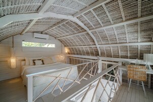 Una habitación con un techo alto y curvo hecho de material tejido, una cama con ropa blanca, una pequeña mesa con una silla y una ventana que proporciona luz natural.