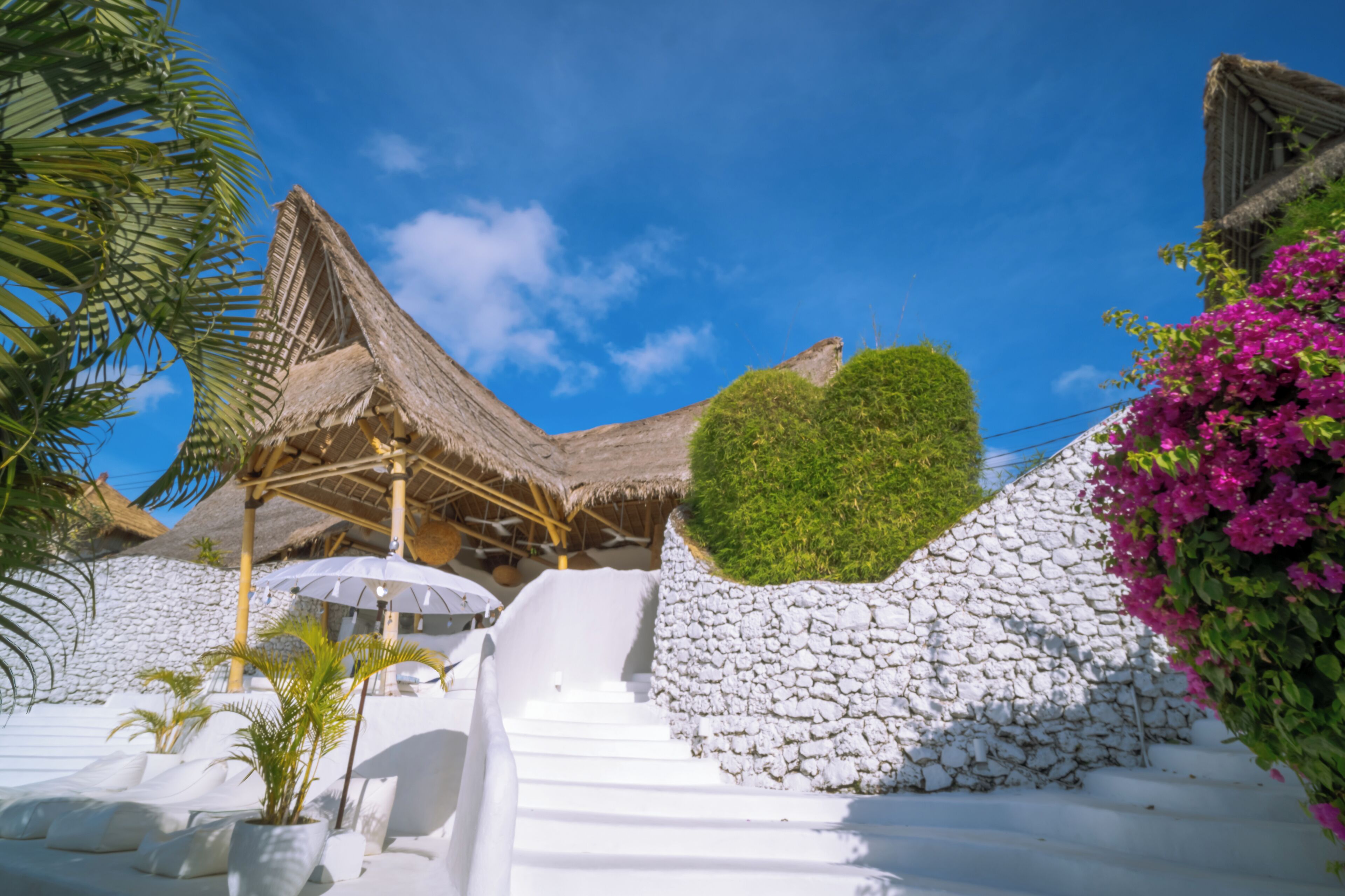 Un resort con una estructura de techo de paja, muros de piedra blanca y una escalera que lleva a un área de descanso blanca.