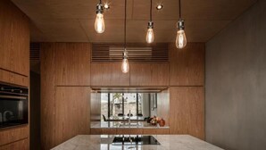 A modern kitchen with wooden cabinetry, a central island with a stainless steel sink, and pendant lighting.