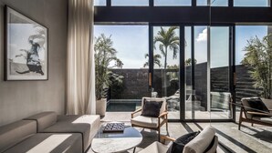 A modern living room with a sofa, chairs, a coffee table, and a view of a pool and palm trees through large glass doors.