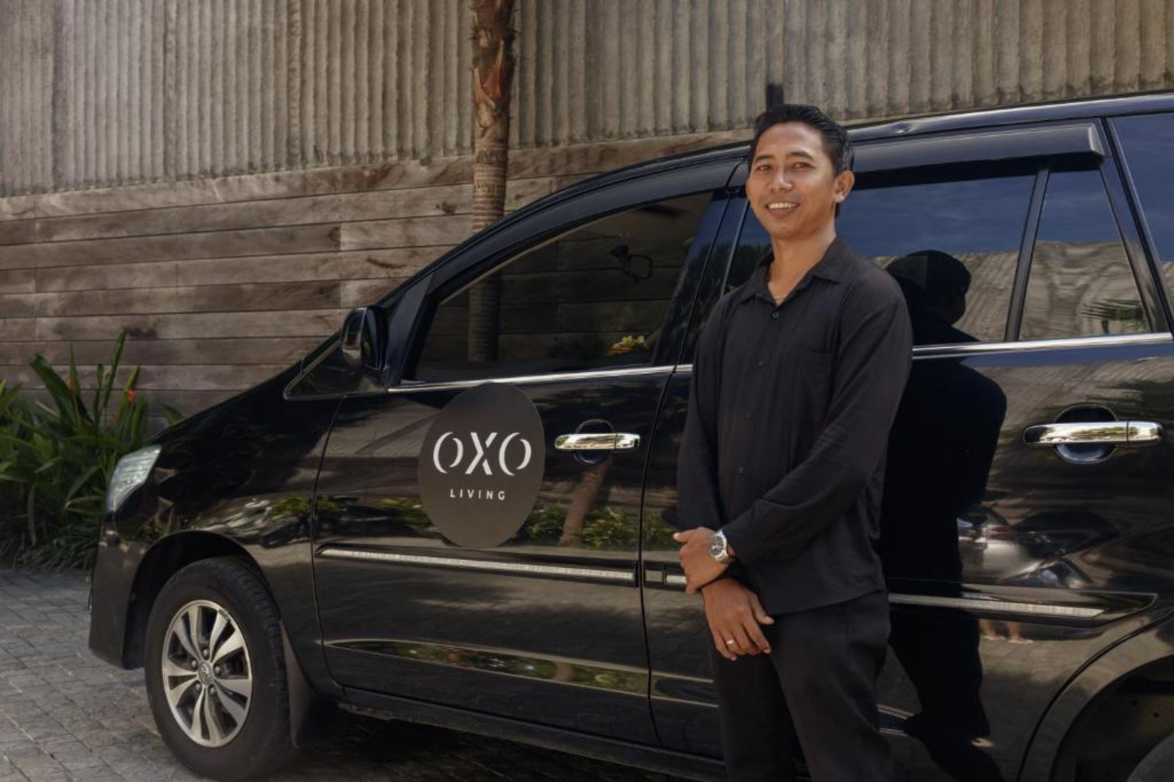 A black van with "Oxo Living" branding parked in front of a corrugated metal wall.