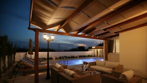 Ein überdachter Außenbereich mit Pool, Korbmöbeln und einer Pergola mit Beleuchtung.