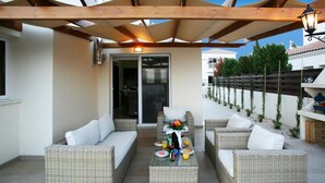 Eine Terrasse im Freien mit Korbmöbeln, einem Tisch, der mit Tellern, Gläsern und einer Blumenkomposition gedeckt ist.