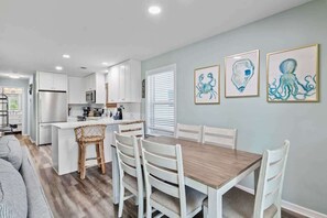 A modern kitchen with white cabinets, a wooden dining table, and a seating area with a sofa.