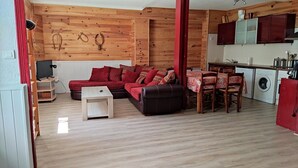 Un espacio habitable compacto con interior de madera, un conjunto de sofá rojo, una mesa de comedor con sillas y una zona de cocina con lavadora.