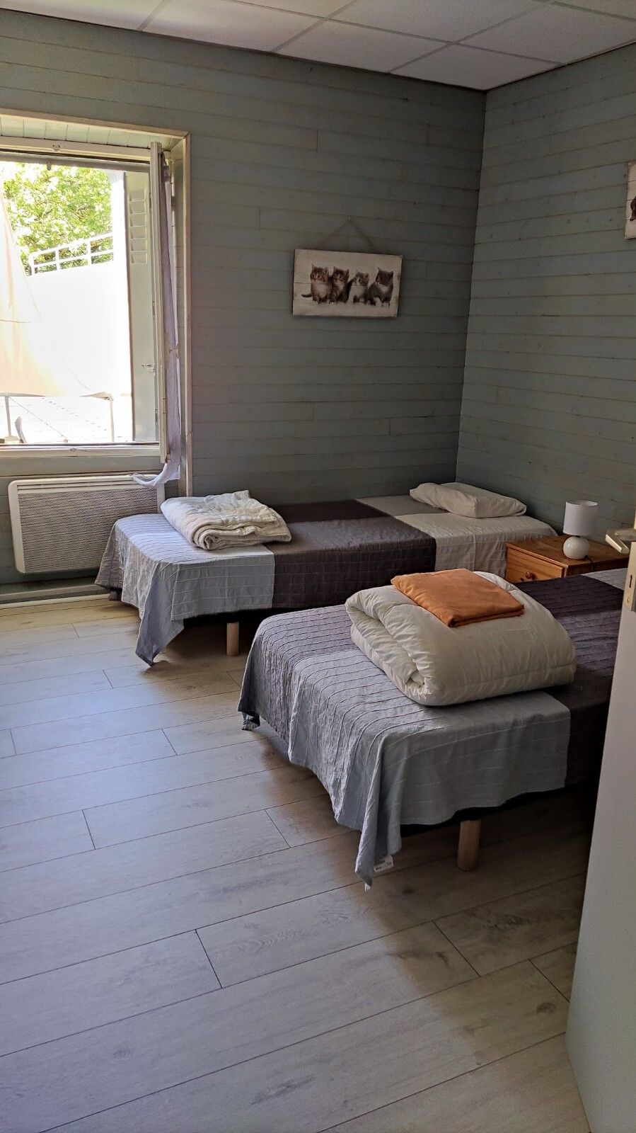 Una habitación con dos camas, un radiador, una ventana y un cuadro en la pared.