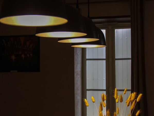 A room with a window, a wall-mounted lamp, and a vase with dried plants.