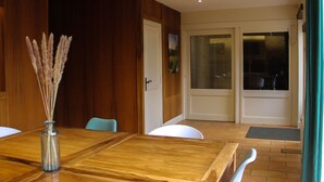 Un coin repas avec une table en bois, des chaises, un vase contenant des plantes séchées et une porte donnant sur une autre pièce.