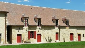 Un bâtiment en pierre doté de nombreuses fenêtres à cadre rouge et d’un toit recouvert de tuiles.