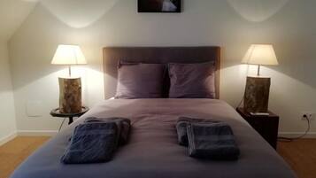 Un lit bien fait, avec une tête de lit, deux lampes de chevet et un tableau encadré au-dessus du lit.