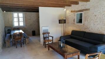 Un salon de style rustique avec un canapé noir, des chaises en bois, une table basse et un mur en pierre.