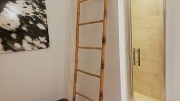Une échelle en bois appuyée contre un mur, un banc en bois et une porte en verre donnant sur une pièce carrelée.