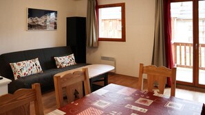A cozy living room with a sofa, a dining table, and chairs. There is a window with curtains, a radiator, and a wall-mounted speaker. - Duplex apt for 8, Pool, Pets allowed - Les Orres 1800 (Les Orres)