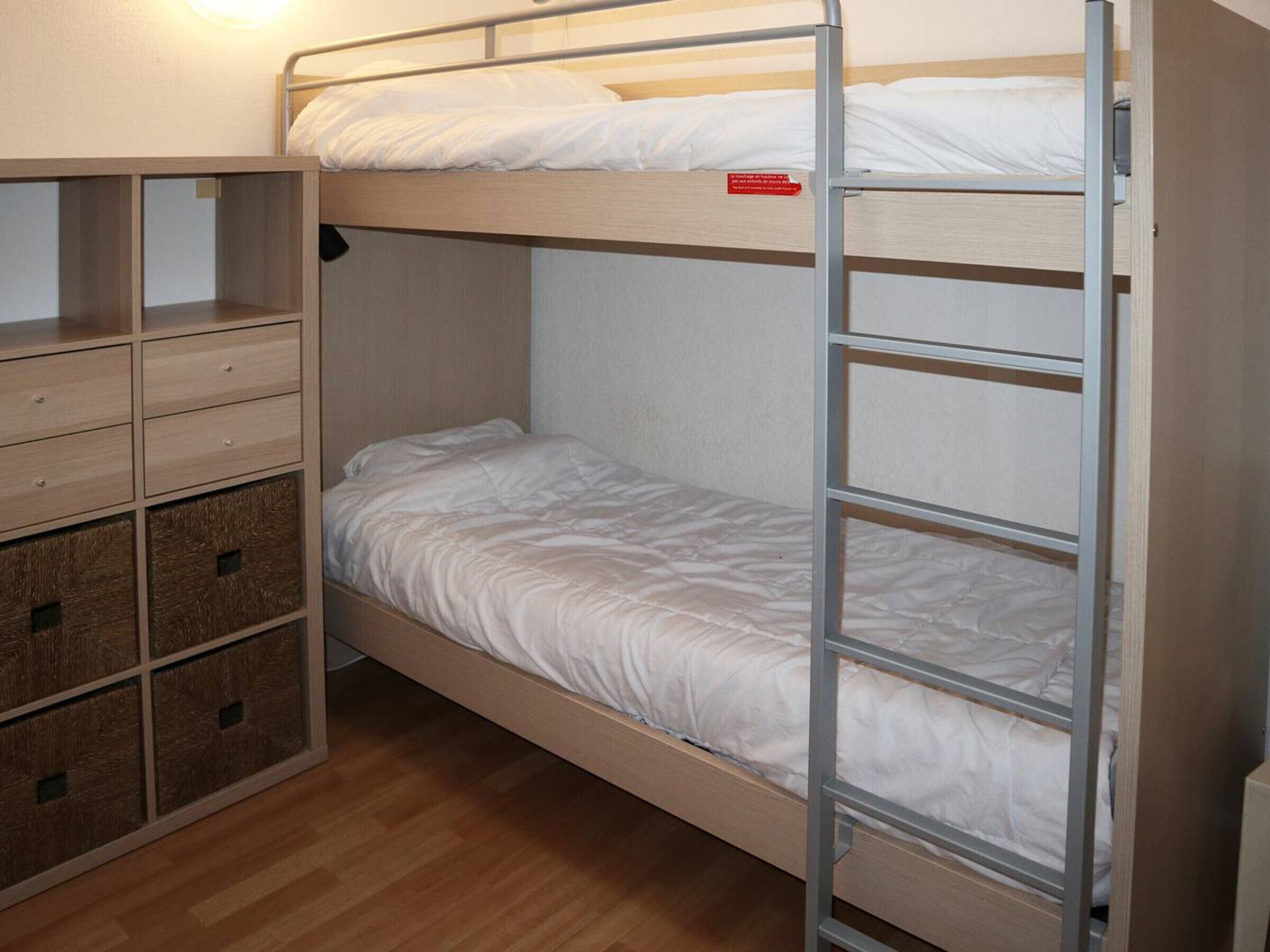 A bunk bed with a wooden frame and a metal ladder. There are two drawers with a textured surface on the left side.