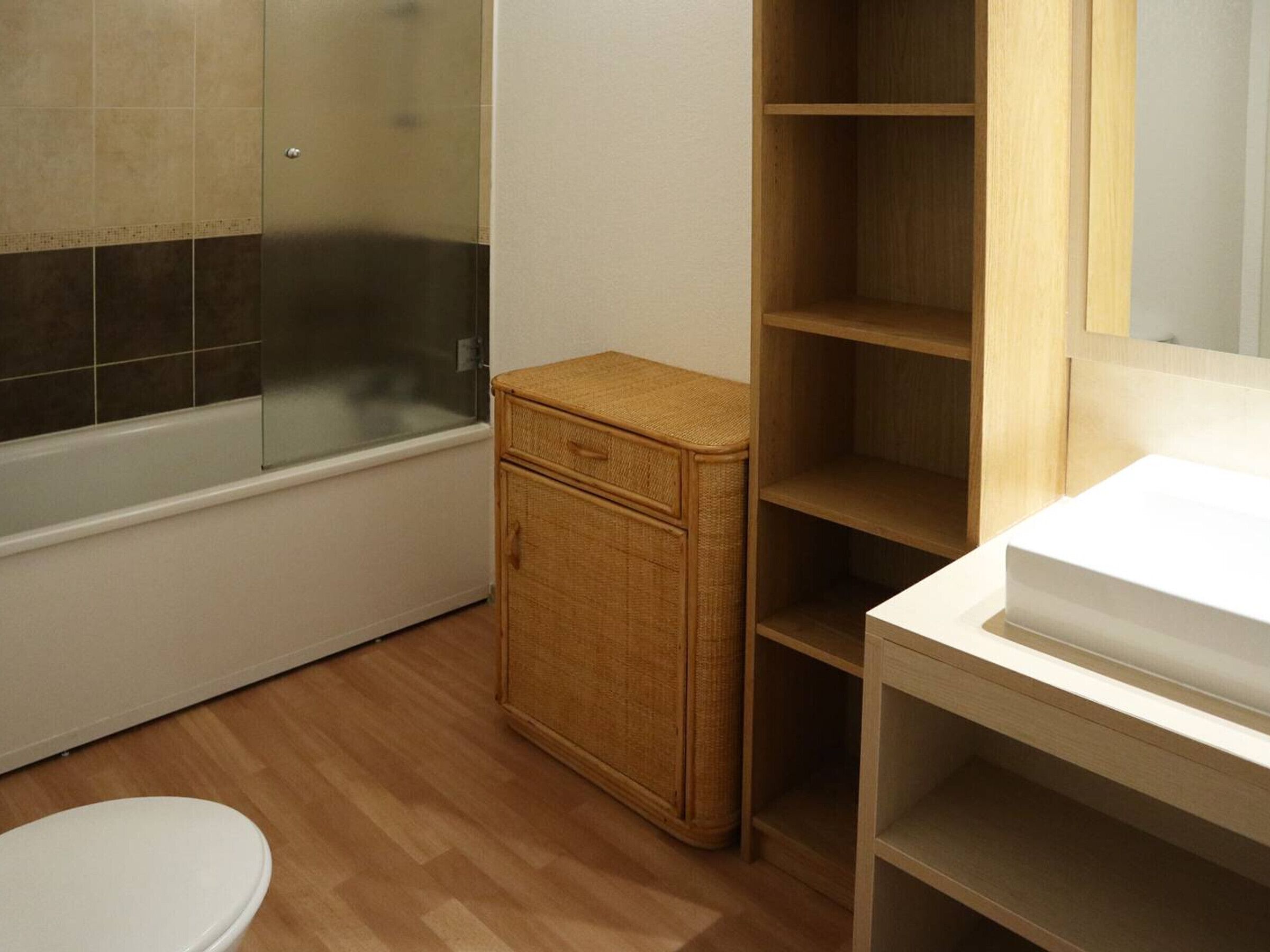 A bathroom with a white toilet, a wooden cabinet, a glass shower enclosure, and a wooden vanity with a mirror.
