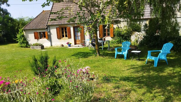 Una casa con tetto in tegole, un prato e due sedie blu.