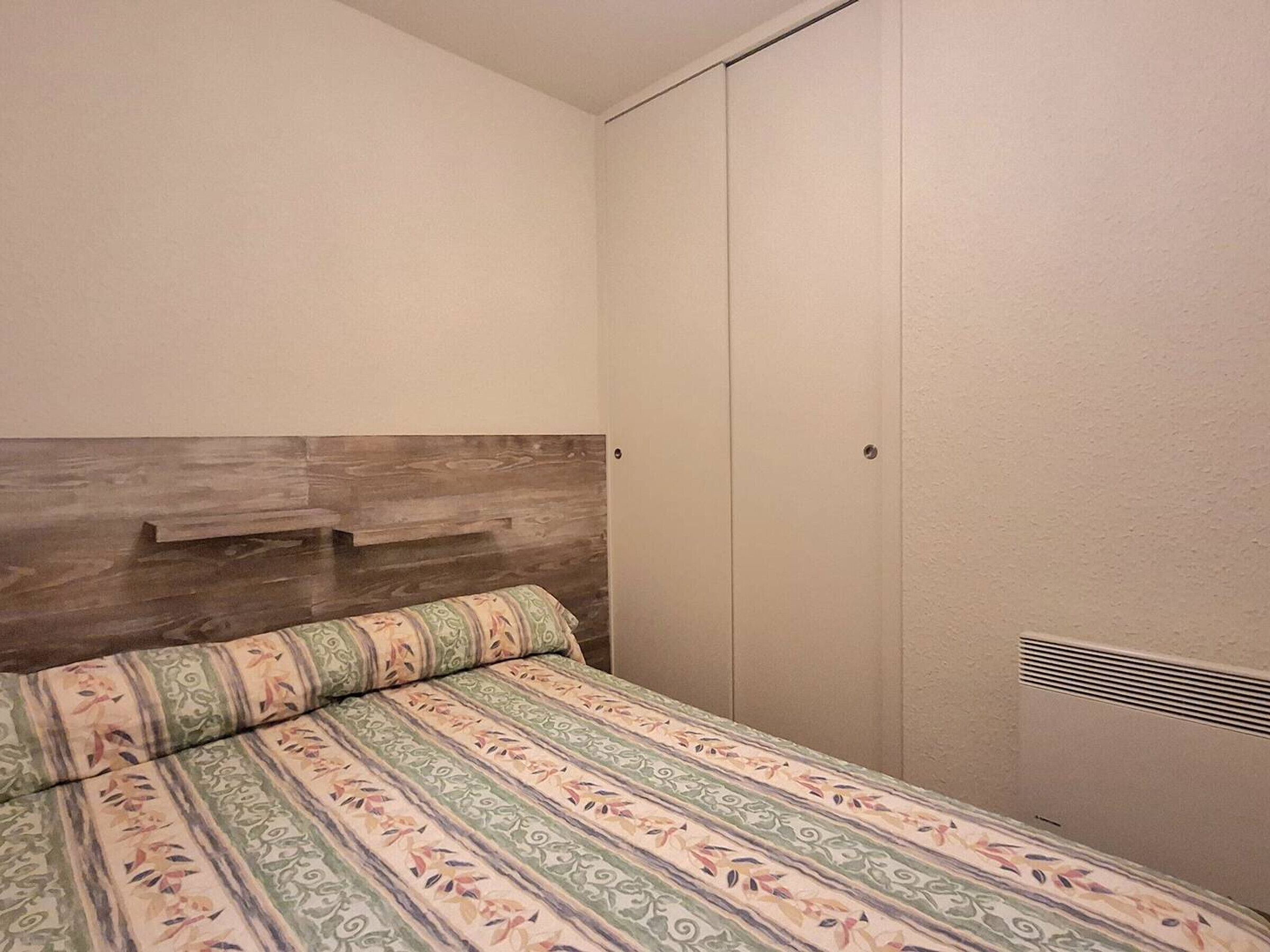 A bedroom with a bed, a wardrobe, and a wooden headboard.