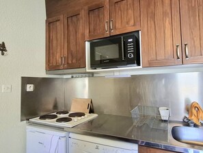 A compact kitchen with wooden cabinets, a stainless steel range, a microwave, a dishwasher, and a sink with a dish rack. - Cozy 3-room apartment for 4 people with balcony near slopes (Bolquère-Pyrénées 2000)