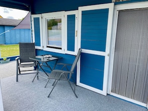 Ein überdachter Patio-Bereich mit Tisch und Stühlen, einer Schiebetür und einem Fenster.