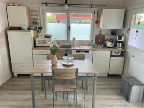 A compact kitchen with a dining table, chairs, a microwave, a coffee maker, and a window with blinds. - Haffglück Vacation Home - Vacation Home (Ueckermünde)