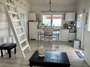 Eine kompakte Küche mit Essbereich, weißen Schränken, einem kleinen Kühlschrank und einem Holztisch mit Vase und Kerzenhaltern.