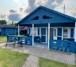 Ein blaues Gebäude mit einer überdachten Terrasse, Sitzgelegenheiten im Freien und einem Kiesweg.