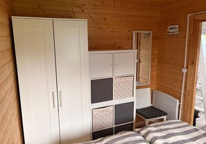 A wooden interior with a wardrobe, a small stool, and a bed with striped bedding. - Haffglück Vacation Home - Vacation Home (Ueckermünde)