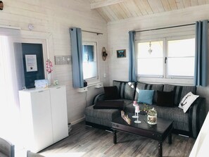 Ein Zimmer mit einer Couch, einem Couchtisch, einer kleinen Kommode und einem Fenster mit Vorhängen.