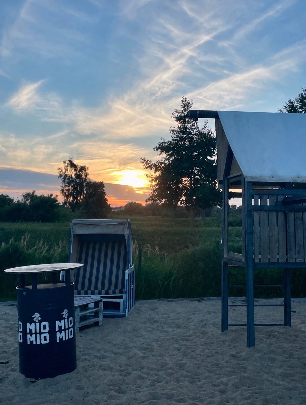 A beach scene with a sunset, a covered seating area, and a trash bin.