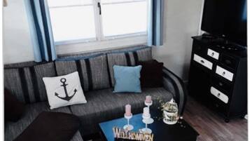 Ein Wohnzimmer mit einer Couch, einem Couchtisch, einem Fernseher und einem Fenster mit Vorhängen.