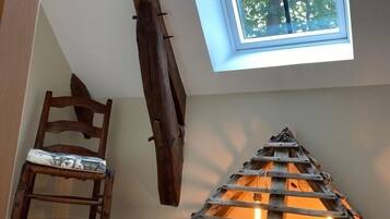 Une chambre à coucher aménagée dans un grenier, avec un plafond en pente, une lucarne, une échelle en bois et une chaise.